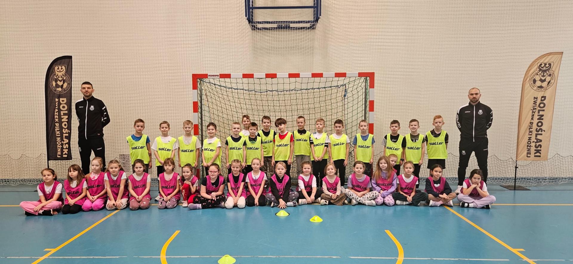 Uczniowie z trenerami stoja na tle bramki