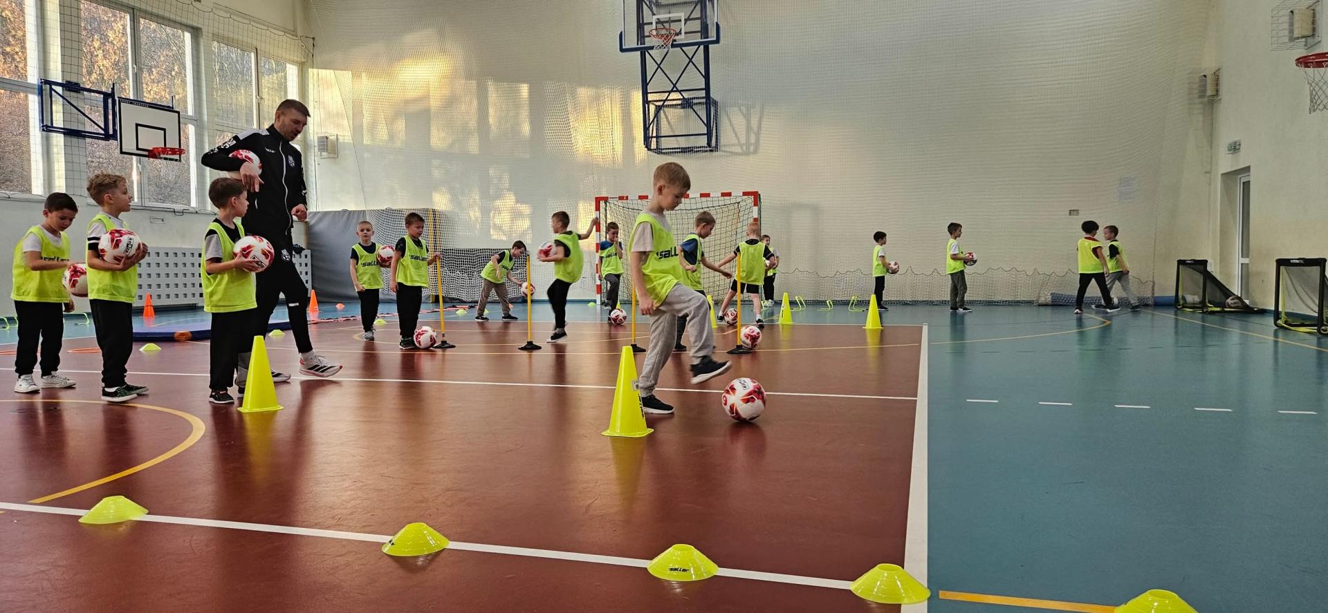 Dzieci wykonuja ćwicznenia z piłką do nogi.